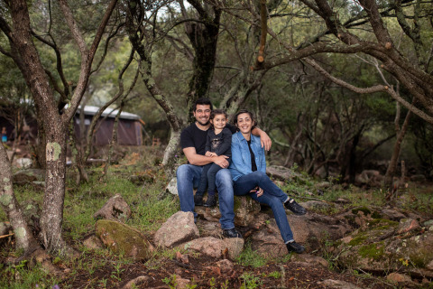 Een gezin zit samen op stenen in het bos bij Feather Down Figari Corsica vakantiepark op Corsica, Frankrijk.