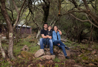 Een gezin zit samen op stenen in het bos bij Feather Down Figari Corsica vakantiepark op Corsica, Frankrijk.