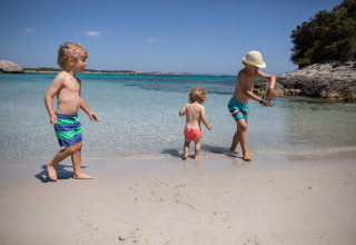 Tre børn leger på sandet ved stranden i Feather Down Figari Corsica, et feriepark i Frankrig.