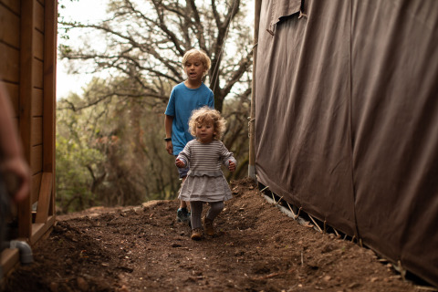 Dos niños juegan al aire libre entre tiendas y árboles en el parque vacacional Feather Down Figari Corsica, Francia.
