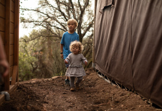 Twee kinderen spelen buiten tussen tenten en bomen in het Feather Down Figari Corsica vakantiepark, Frankrijk.