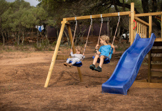 Two children play on swings and a slide at a playground at Feather Down Figari Corsica, France.