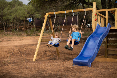 Dos niños juegan en columpios y un tobogán en un parque infantil en Feather Down Figari Córcega, Francia.