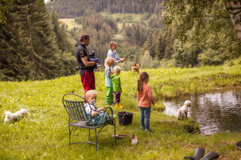 Familia pescando junto a un estanque rodeados de naturaleza y montañas en Feather Down Hilserhof, Alemania.