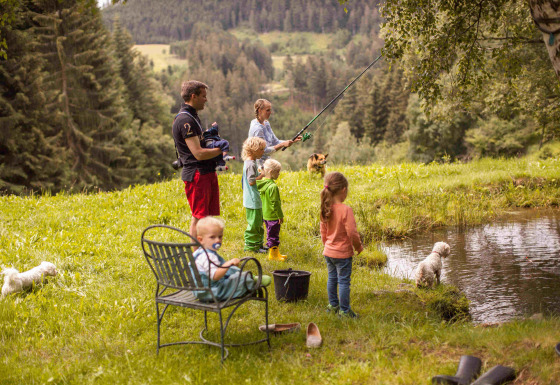 Familie fisker ved en dam omgivet af natur og bjerge i ferieparken Feather Down Hilserhof, Tyskland.