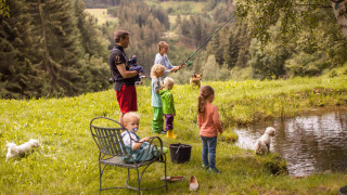 Familia pescando junto a un estanque rodeados de naturaleza y montañas en Feather Down Hilserhof, Alemania.