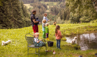 Familia pescando junto a un estanque rodeados de naturaleza y montañas en Feather Down Hilserhof, Alemania.
