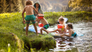 Niños juegan cerca de un estanque rodeado de naturaleza, un punto destacado de Feather Down Hilserhof en Alemania.