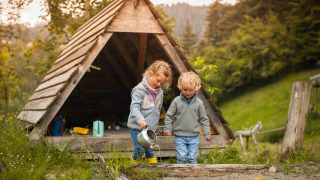 Dos niños juegan frente a una cabaña de madera en Feather Down Hilserhof, parque de vacaciones en Baden-Württemberg.