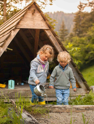 Dos niños juegan frente a una cabaña de madera en Feather Down Hilserhof, parque de vacaciones en Baden-Württemberg.