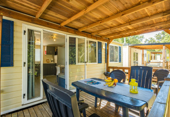 Overdekt terras van Mobile home Capri met plastieken tafel, stoelen en zicht op de keuken binnen.