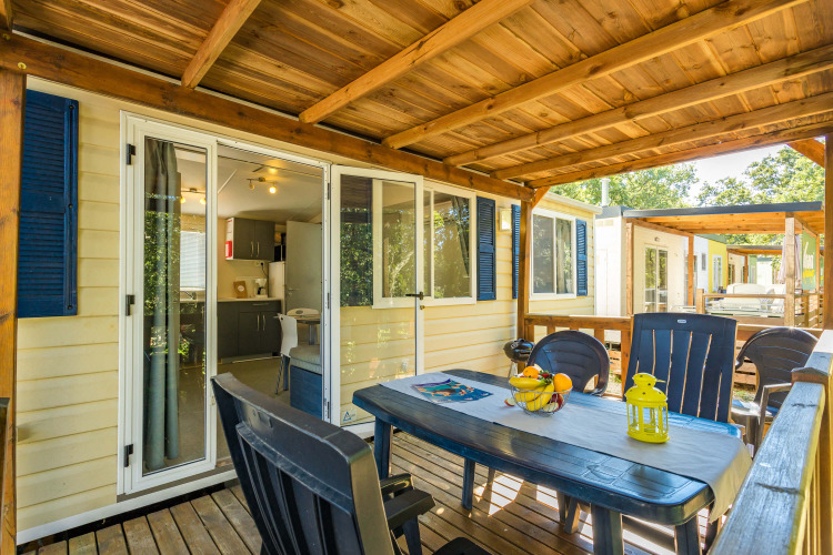 Mobile Home Capri covered wooden terrace with table, chairs, open sliding doors and kitchen view.
