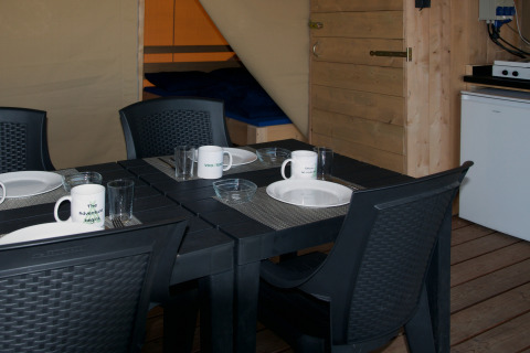 Mesa de comedor dentro de tienda safari, sillas negras, mesa puesta y cama en Minicamping de Vrolijke Flierefluiter.