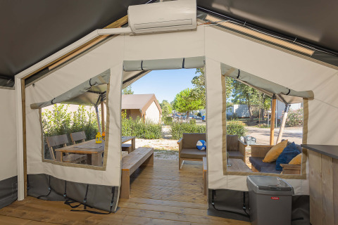 Vue intérieure d'une tente safari Comfort climatisée avec terrasse en bois et coin salon extérieur.
