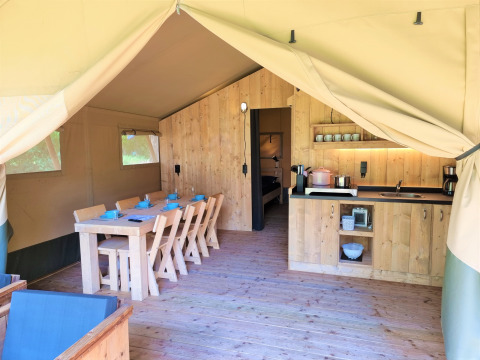 Intérieur d’une tente safari de luxe avec meubles en bois, table à manger, cuisine et vue sur la chambre.