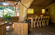 Interieur van een safaritent met houten zitmeubilair en eettafel bij Løkken Klit Camping, Denemarken.