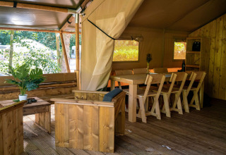 Interieur van een safaritent met houten zitmeubilair en eettafel bij Løkken Klit Camping, Denemarken.