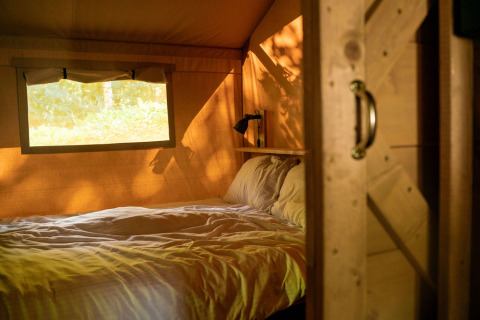 Gemütlicher Schlafbereich mit Doppelbett im Safarizelt mit Fenster bei Løkken Klit Camping, Dänemark.