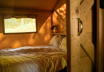 Gemütlicher Schlafbereich mit Doppelbett im Safarizelt mit Fenster bei Løkken Klit Camping, Dänemark.