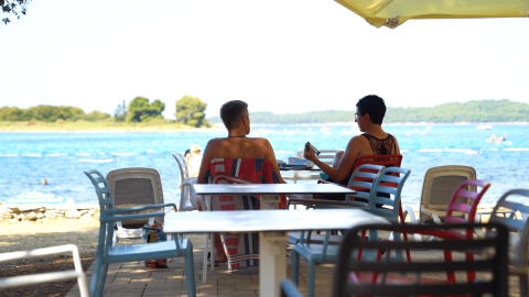 Due persone sedute a un tavolo nel bar sulla spiaggia a Camping Polari, Istria, Croazia.