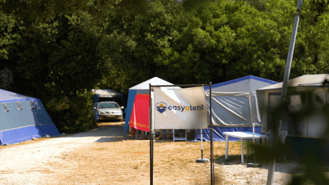 Zona de acampada con tiendas, un cartel de 'easytent' y un coche entre árboles en Camping Polari, Istria.