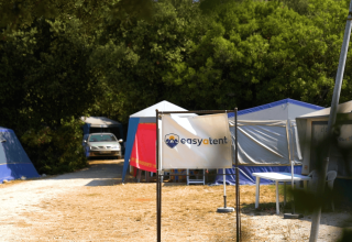 Campingområde med telt, et skilt med 'easytent' og bil, omgivet af grønne træer i Camping Polari, Istrien.