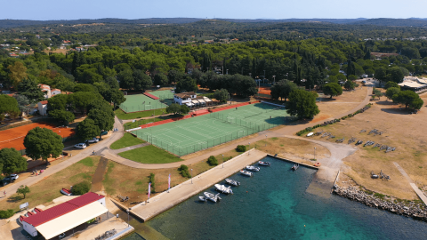 Vista aerea di Camping Polari in Istria, Croazia, con campi sportivi, marina e paesaggio verde rigoglioso.