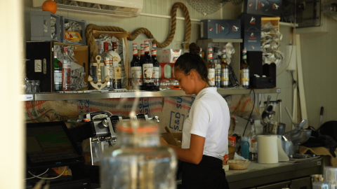 Femme travaillant derrière le bar avec des bouteilles et du matériel au Camping Polari, parc de vacances en Istrie, Croatie.