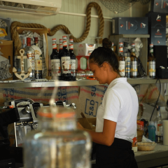Mujer trabajando detrás de la barra con botellas y equipo en Camping Polari, un parque vacacional en Istria, Croacia.