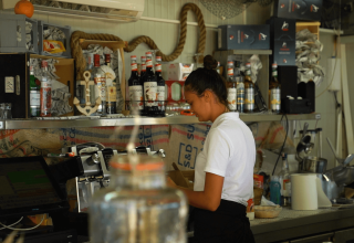 Woman working behind the bar with bottles and equipment at Camping Polari, a holiday park in Istria, Croatia.