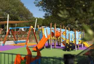 Parco giochi colorato con altalene e scivolo al Camping Polari in Istria, Croazia, circondato dal verde.