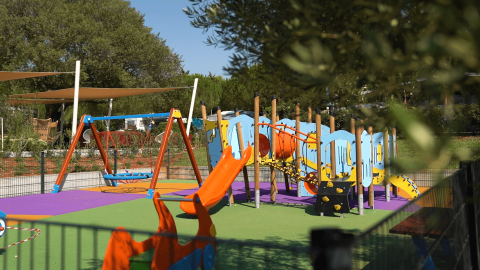 Parco giochi colorato con altalene e scivolo al Camping Polari in Istria, Croazia, circondato dal verde.