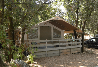 Wooden tent with a porch surrounded by trees at Camping Polari holiday park, Istria, Croatia, on a sunny day.