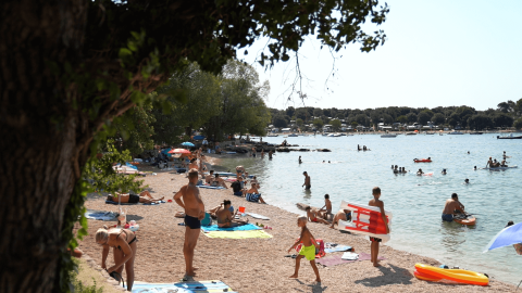 Escena de playa en Camping Polari, Istria, Croacia, con veraneantes tomando el sol y nadando en el mar.