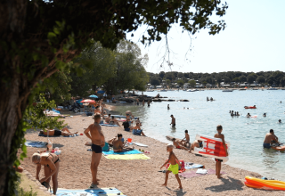 Escena de playa en Camping Polari, Istria, Croacia, con veraneantes tomando el sol y nadando en el mar.