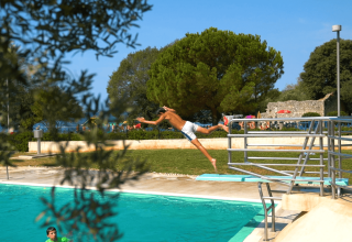 Dreng springer fra vippe og hopper i poolen på Camping Polari i Istrien, Kroatien, omgivet af grøn natur.