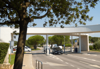 Entrance of Camping Polari holiday park in Istria, Croatia, with cars, trees, and modern white structure.