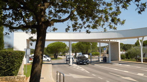 Entrance of Camping Polari holiday park in Istria, Croatia, with cars, trees, and modern white structure.