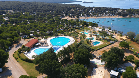 Vista dall'alto di Camping Polari in Istria, Croazia, con piscine, aree verdi e la costa vicina.