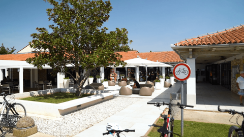 Zona exterior en Camping Polari, Istria, Croacia, con terraza de café, señal de prohibido bicicletas y árboles frondosos.