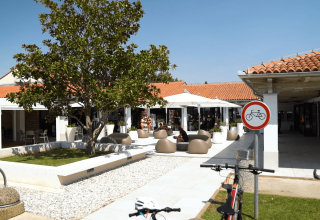 Outdoor communal area at Camping Polari in Istria, Croatia, with café seating, bike ban sign, and leafy trees.