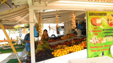 Bancarella di frutta e verdura a Camping Polari, Istria, Croazia, con clienti e cartello del formaggio.