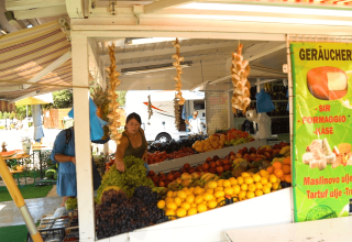 Puesto de frutas y verduras en Camping Polari, Istria, Croacia, con gente comprando y cartel de queso.