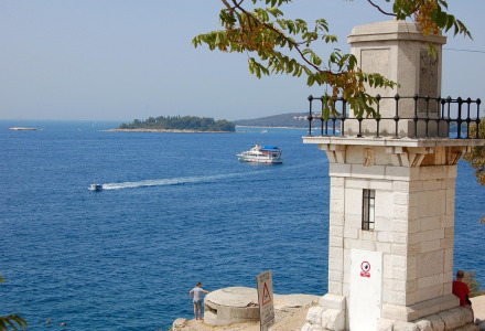 Vista al mar con faro, barcos e islas, tomada desde un parque vacacional con alojamientos glamping.