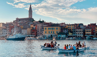 Casas coloridas y barcos en Rovinj, Croacia, con personas disfrutando del agua en un día soleado.