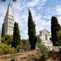 Iglesia histórica con torre alta entre árboles y cielo azul, vista desde un parque vacacional de glamping.