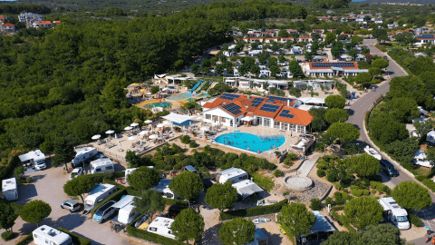 Vista aérea del Camping Krk en Croacia con piscina central, autocaravanas y abundante vegetación.