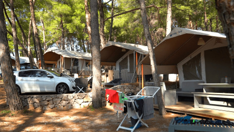 Tende e bungalow tra pini a Camping Krk, con auto parcheggiata e stendibiancheria in Croazia.