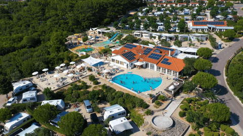 Vista aerea del Camping Krk, con piscina, camper, tanto verde e pannelli solari in Croazia.