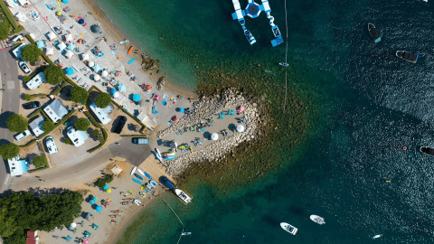 Vista aerea di Camping Krk in Croazia con spiaggia, camper, ombrelloni e barche sull’acqua limpida.
